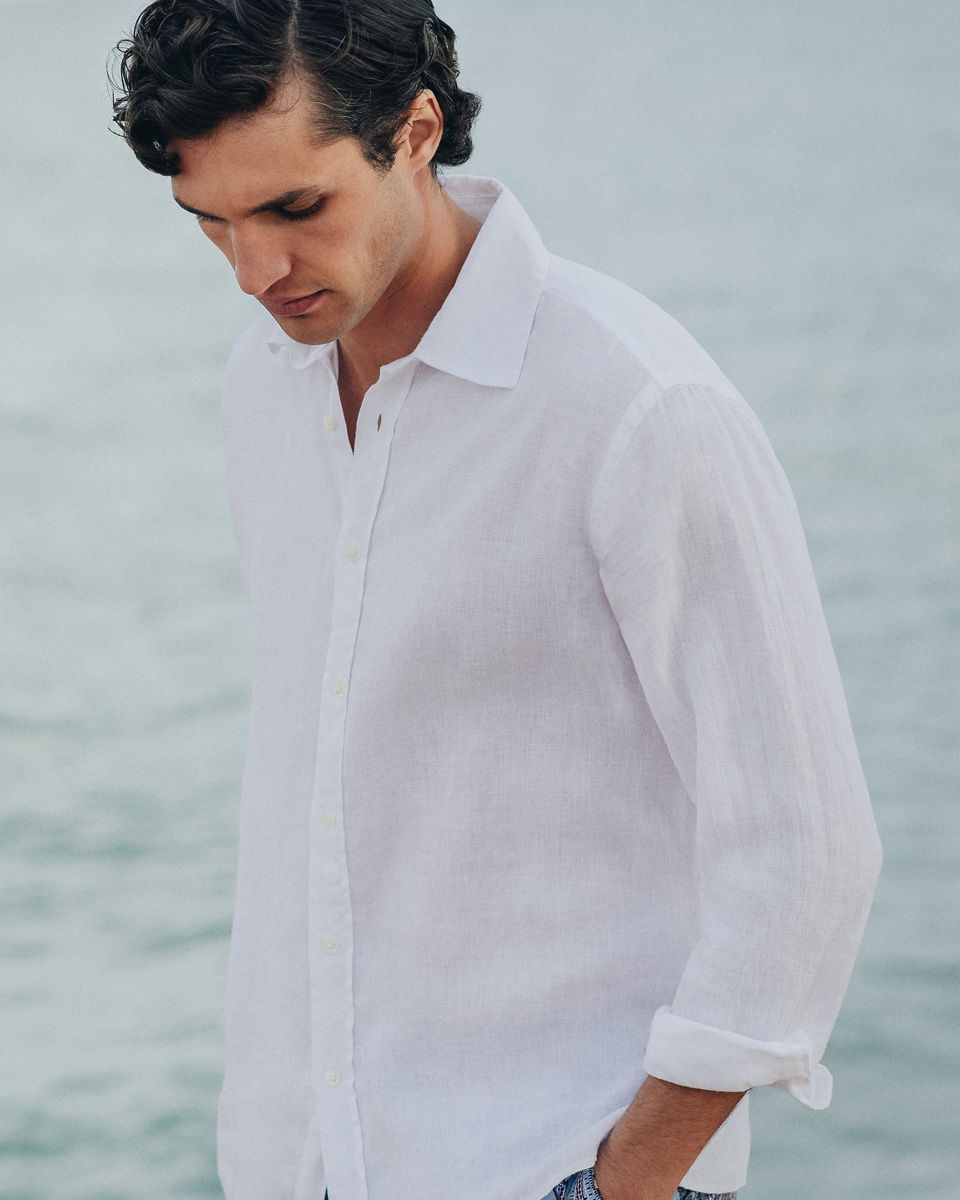 Vor Meereskulisse stehender Herr mit weißem Hemd mit hochgekrempelten Ärmeln Vor Meereskulisse stehender Herr mit weißem Hemd mit hochgekrempelten Ärmeln