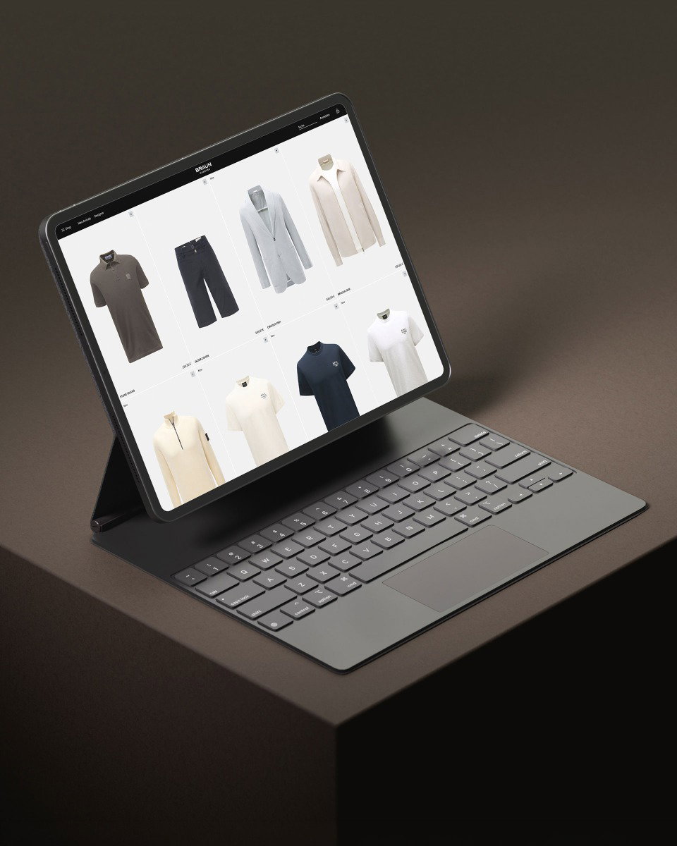 Tablet mit Tastatur auf braunem Untergrund, Bildschirm zeigt Online-Shop mit Kleidung wie Poloshirt, Shorts, Blazer und T-Shirts.