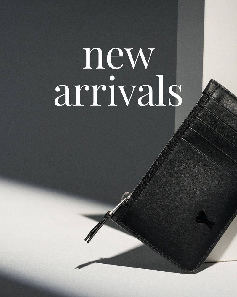 Black leather cardholder with zipper and multiple card slots leaning against a wall, with 'new arrivals' text above.