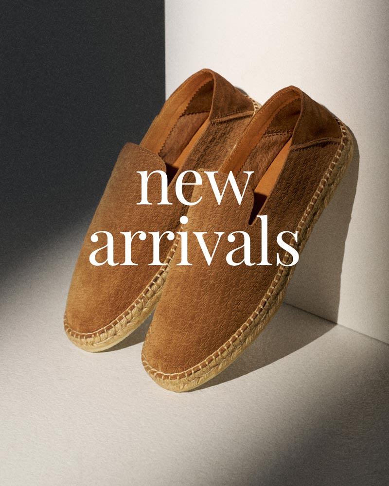 Braune Wildleder-Espadrilles mit Bastsohle, schräg an weiße Wand gelehnt, Text 'new arrivals' in weiß darüber.