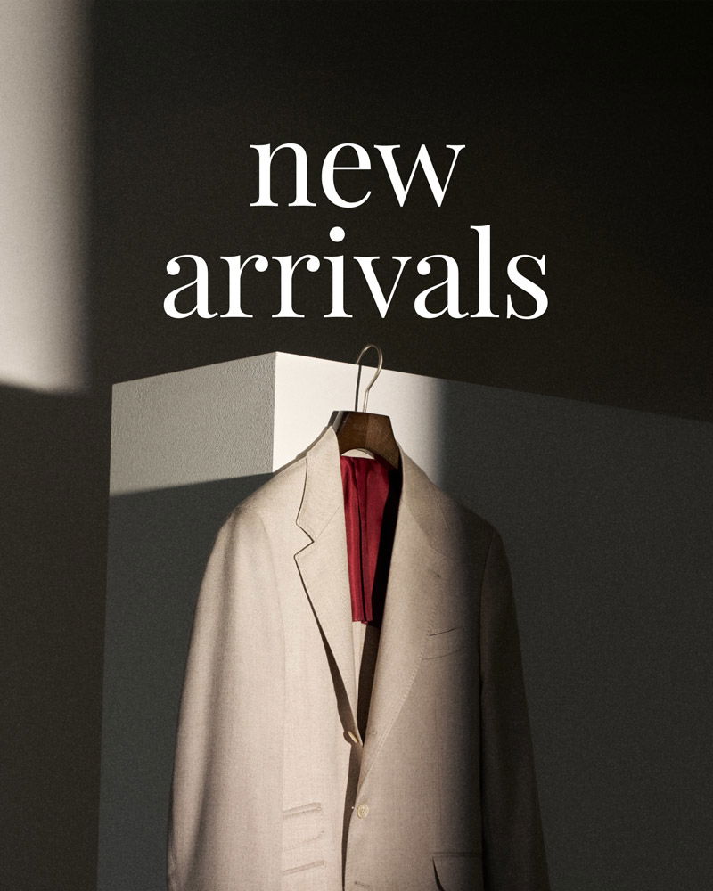 Beige suit jacket hanging on a wooden hanger with a red inner lining, spotlighted against a dark background with 'new arrivals' text.