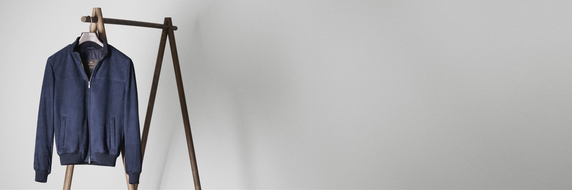 Dunkelblaue Jacke mit Reißverschluss hängt an einem braunen Holzkleiderständer vor weißer Wand. Dunkelblaue Jacke mit Reißverschluss hängt an einem braunen Holzkleiderständer vor weißer Wand.