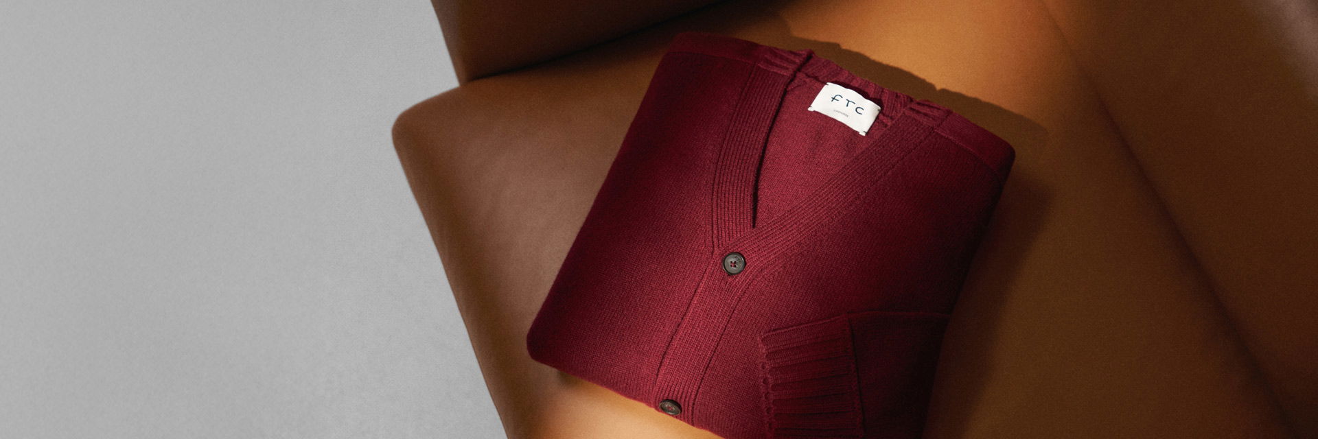 Weinrote, gefaltete Strickjacke mit Knöpfen liegt auf braunem Ledersessel, minimalistisches Ambiente, seitliche Perspektive. Weinrote, gefaltete Strickjacke mit Knöpfen liegt auf braunem Ledersessel, minimalistisches Ambiente, seitliche Perspektive.