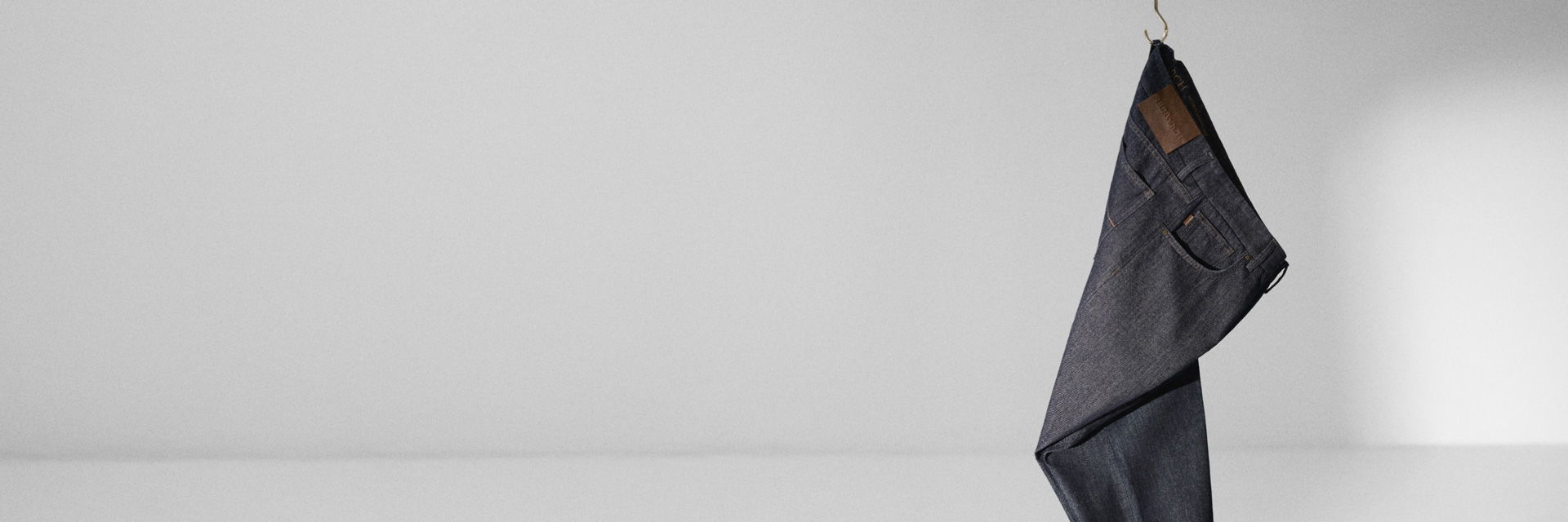 Dunkelblaue Jeans mit sichtbaren Taschen und braunem Leder-Label, hängend vor schlichtem, hellgrauem Hintergrund. Dunkelblaue Jeans mit sichtbaren Taschen und braunem Leder-Label, hängend vor schlichtem, hellgrauem Hintergrund.