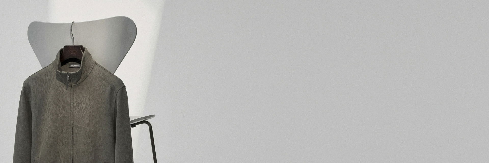 Jacke mit Reißverschluss und Stehkragen in Grau auf einem grauen Stuhl hängend vor weißem Hintergrund. Jacke mit Reißverschluss und Stehkragen in Grau auf einem grauen Stuhl hängend vor weißem Hintergrund.