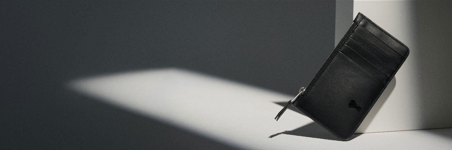 Black leather cardholder with zipper and multiple card slots, angled and lit by a soft light on a light gray surface. Black leather cardholder with zipper and multiple card slots, angled and lit by a soft light on a light gray surface.