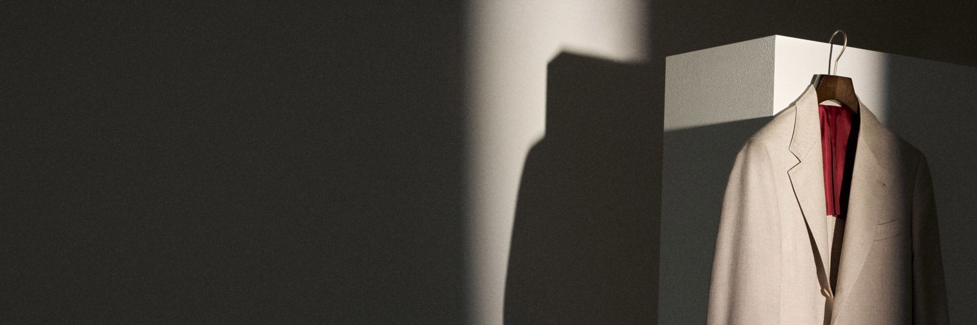 Beige Anzugjacke auf Holzkleiderbügel mit rotem Futter, hängend vor weißem Kubus, Schatten an dunkler Wand. Beige Anzugjacke auf Holzkleiderbügel mit rotem Futter, hängend vor weißem Kubus, Schatten an dunkler Wand.