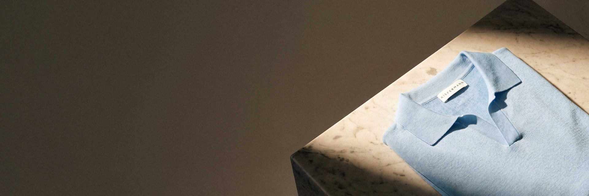 Hellblaues, kurzärmeliges Poloshirt aus feinem Stoff, ordentlich gefaltet auf marmorierter Tischplatte mit Schatten. Hellblaues, kurzärmeliges Poloshirt aus feinem Stoff, ordentlich gefaltet auf marmorierter Tischplatte mit Schatten.