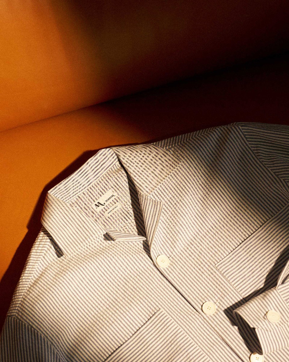 Striped button-up shirt with white and light blue lines laid on an orange surface, showing collar and front buttons.
