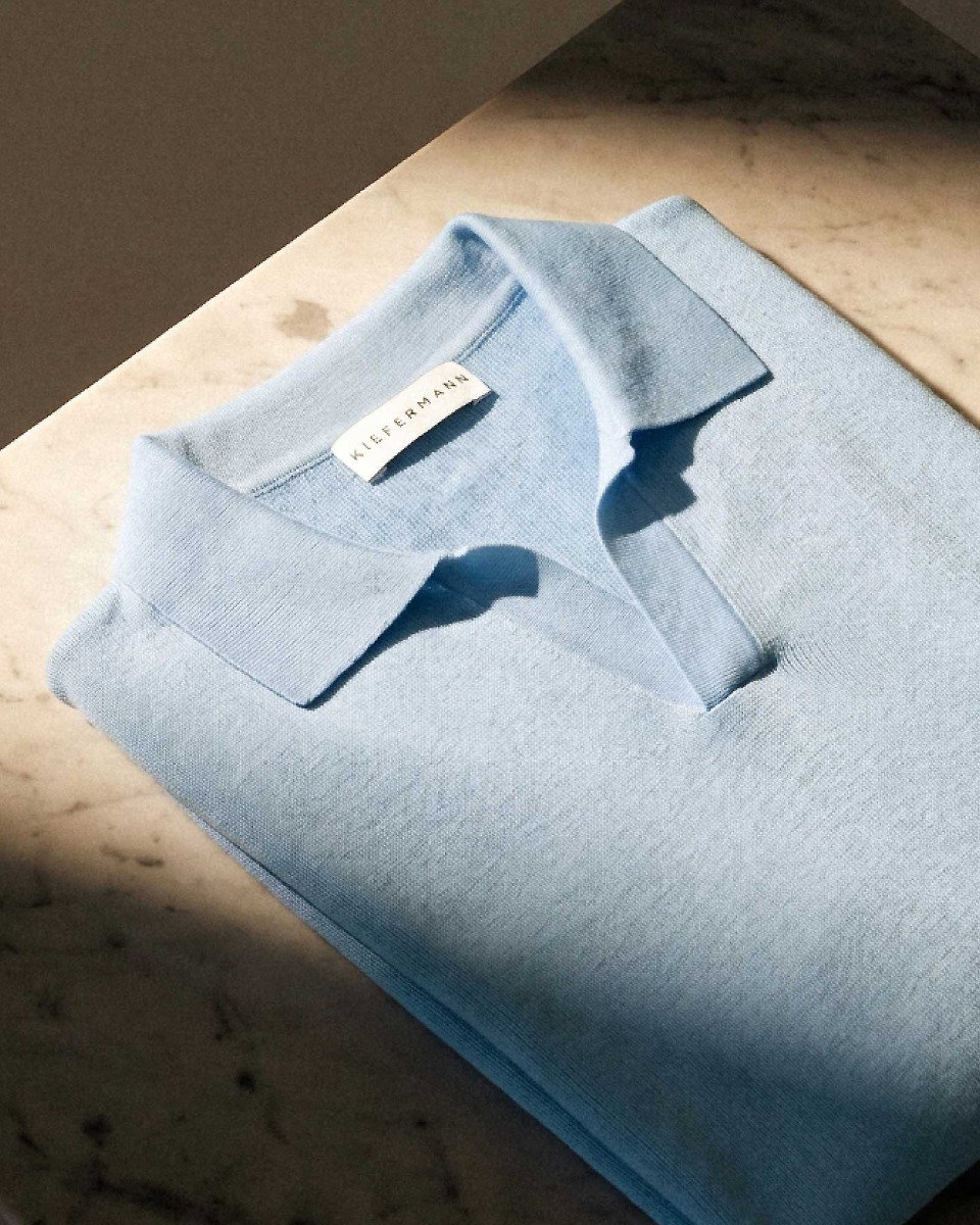 Light blue folded knit polo shirt with a collar and a visible KIEFERMANN label on a marble surface.