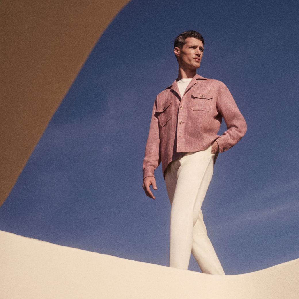 Mann in rosa Jacke und weißer Hose steht vor blauem Himmel, umgeben von weißen und braunen architektonischen Formen. Mann in rosa Jacke und weißer Hose steht vor blauem Himmel, umgeben von weißen und braunen architektonischen Formen.