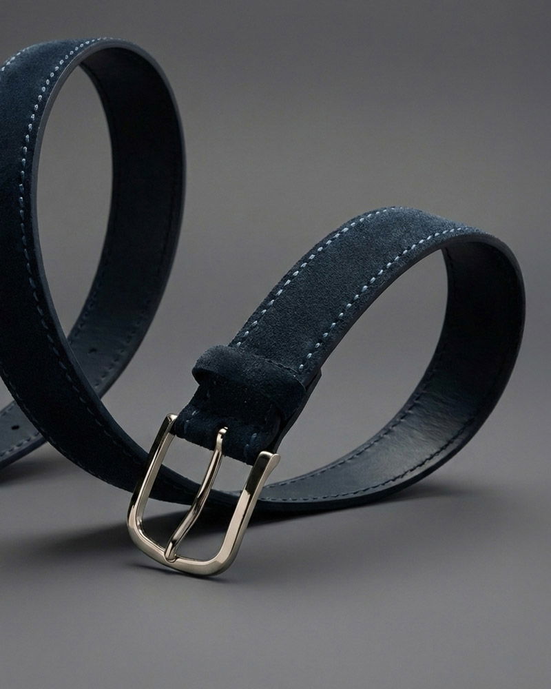 Dunkelblauer Ledergürtel mit silberner Metallschließe und feiner Naht, auf grauem Hintergrund elegant geschwungen.