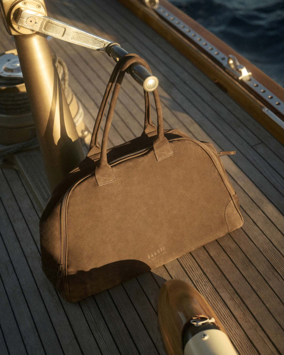 Brown leather duffel bag with handles resting on wooden deck of a boat near metal railing and nautical equipment.