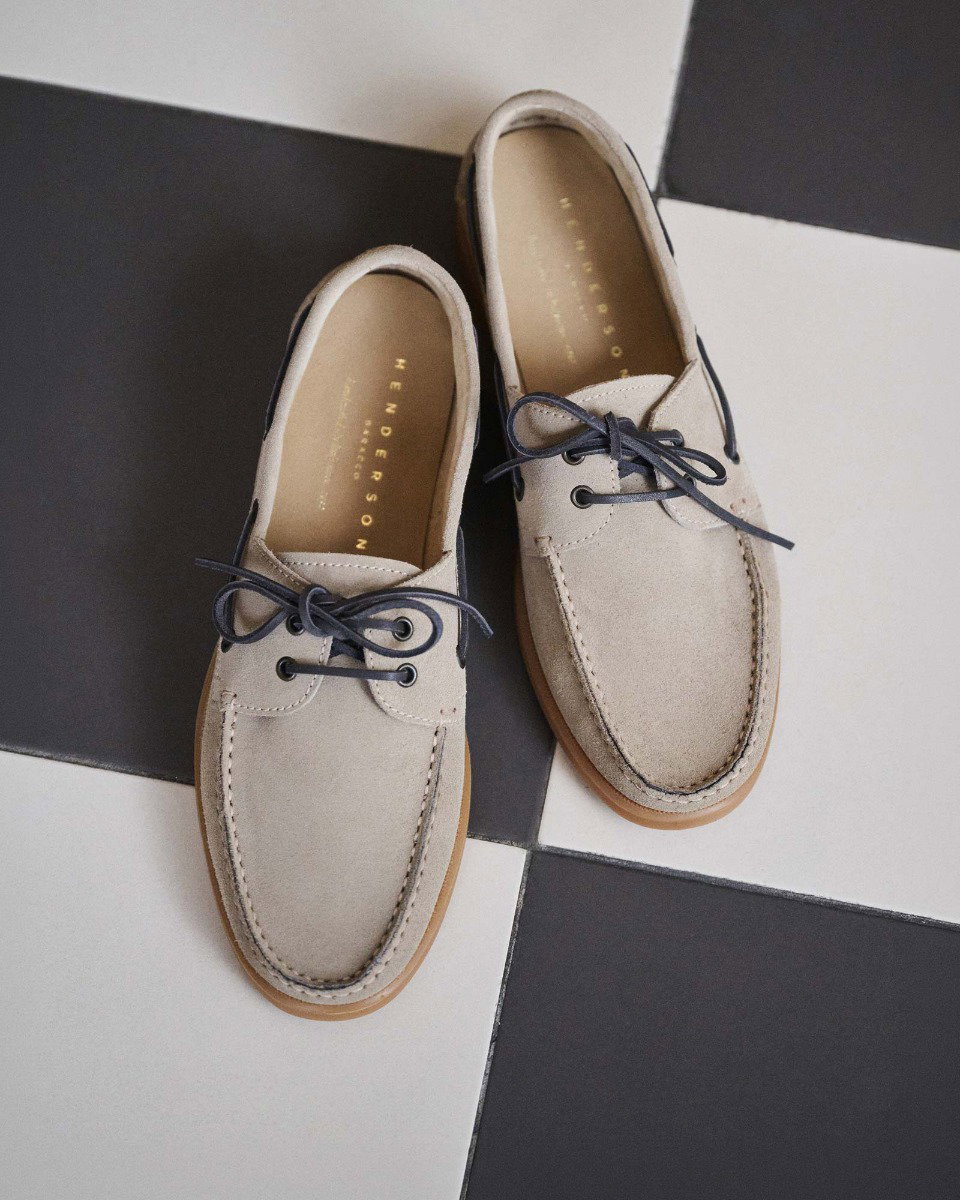 Beige suede boat shoes with dark laces and brown soles on a black and white checkered floor.