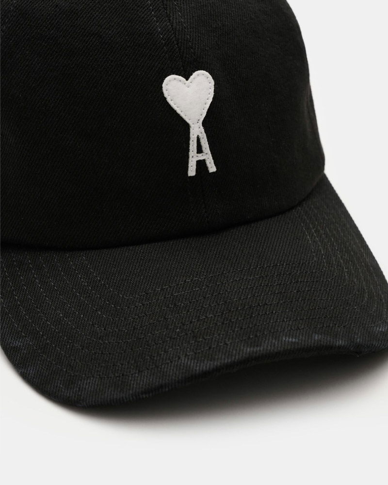 Schwarze Baseballcap mit weißem aufgesticktem Herz und Buchstabe 'A' auf der Vorderseite, Nahaufnahme.