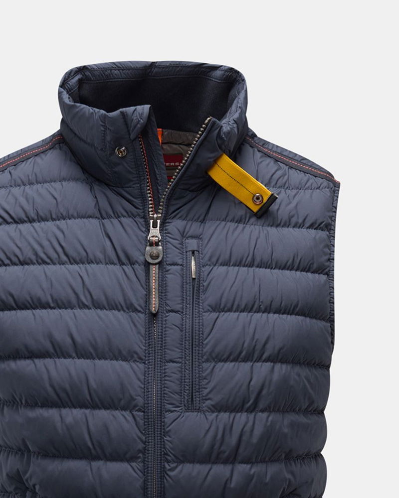 Steppweste in Dunkelblau mit Stehkragen, Frontreißverschluss, Brusttasche und gelbem Stofflaschen-Detail am Kragen.