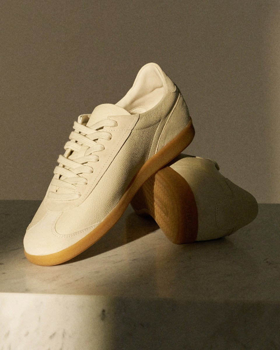 Pair of off-white leather sneakers with gum rubber soles displayed on a marble surface against a neutral background.