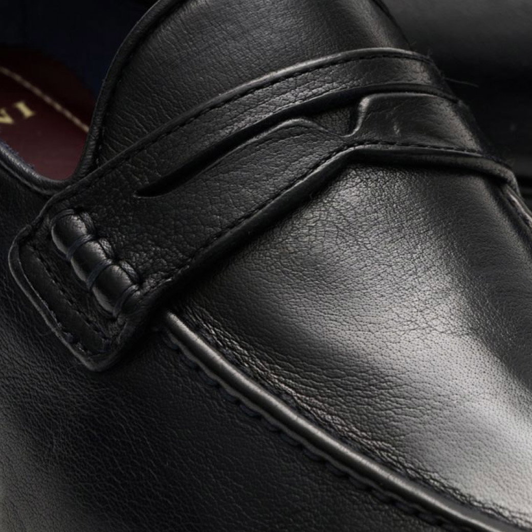 Schwarzer Lederschuh mit dezenter Naht und dekorativem Riemen, Nahaufnahme zeigt feine Lederstruktur und Verarbeitung.