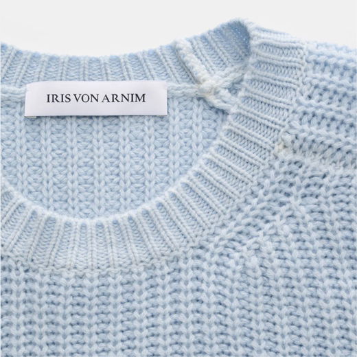 Hellblauer, grob gestrickter Pullover mit Rundhalsausschnitt und weißem Markenlabel 'IRIS VON ARNIM' am Kragen.