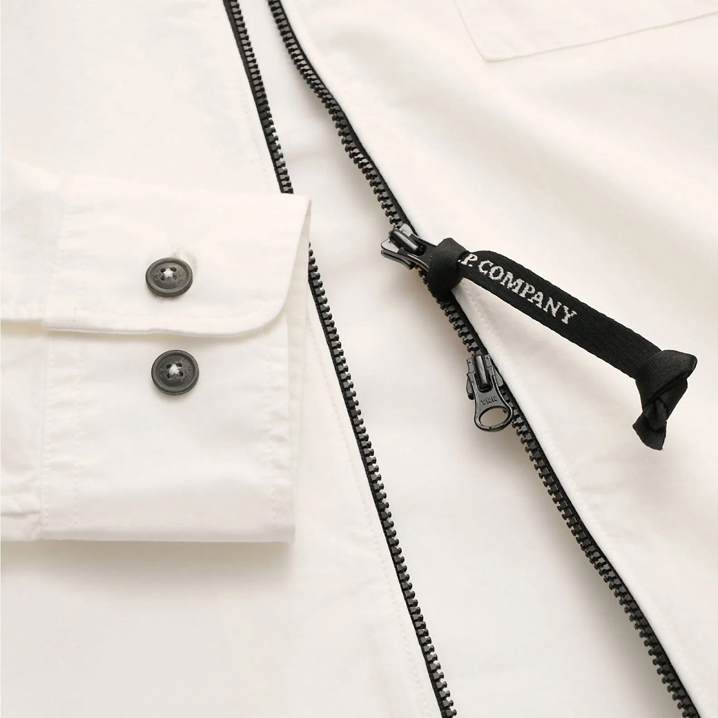 Weißes Kleidungsstück mit schwarzen Knöpfen am Ärmel und schwarzem Reißverschluss mit Zipper-Anhänger 'P. COMPANY'.