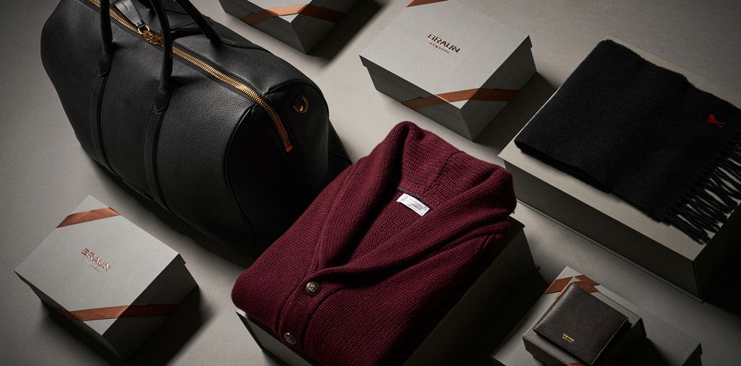 Schwarze Ledertasche, graue Geschenkboxen mit Braun-Logo, rote Strickjacke, schwarzer Puma-Schal und braunes Portemonnaie. Schwarze Ledertasche, graue Geschenkboxen mit Braun-Logo, rote Strickjacke, schwarzer Puma-Schal und braunes Portemonnaie.