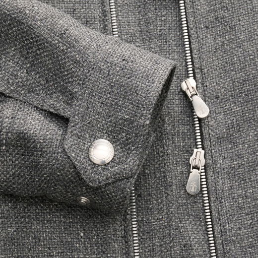 Grauer Wollstoff mit feiner Struktur, silberner Druckknopf am Ärmel und zwei silberne Reißverschluss-Schieber an einer Jacke.