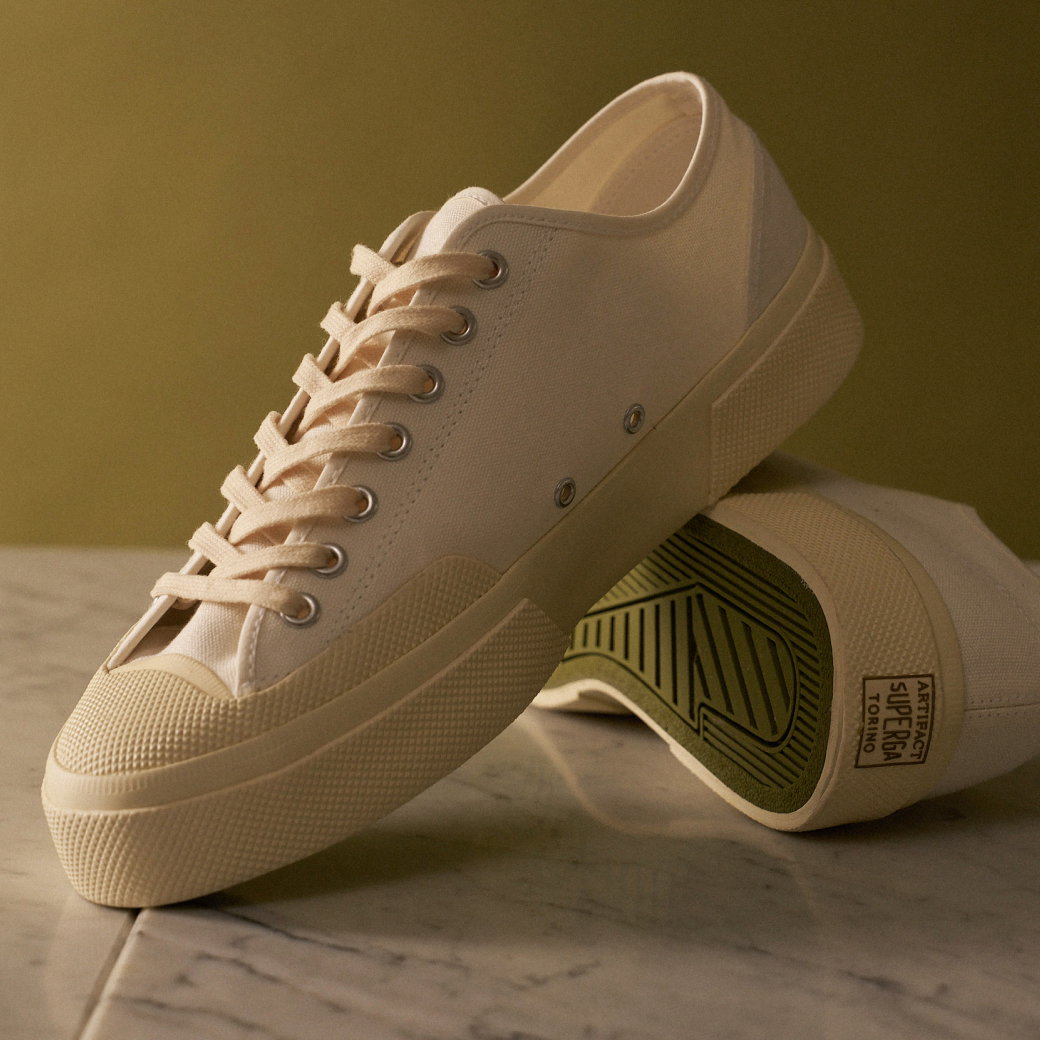 Beige Sneaker aus Canvas mit Gummisohle und Schnürsenkeln, ein Schuh liegt auf der Marmoroberfläche, der andere zeigt die Sohle.