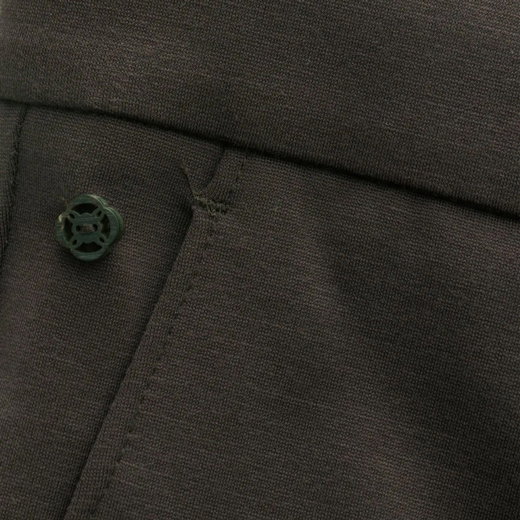 Dunkelbrauner Stoff mit sichtbarer Naht, Tasche und grünem Knopf mit rundem, dekorativem Design.