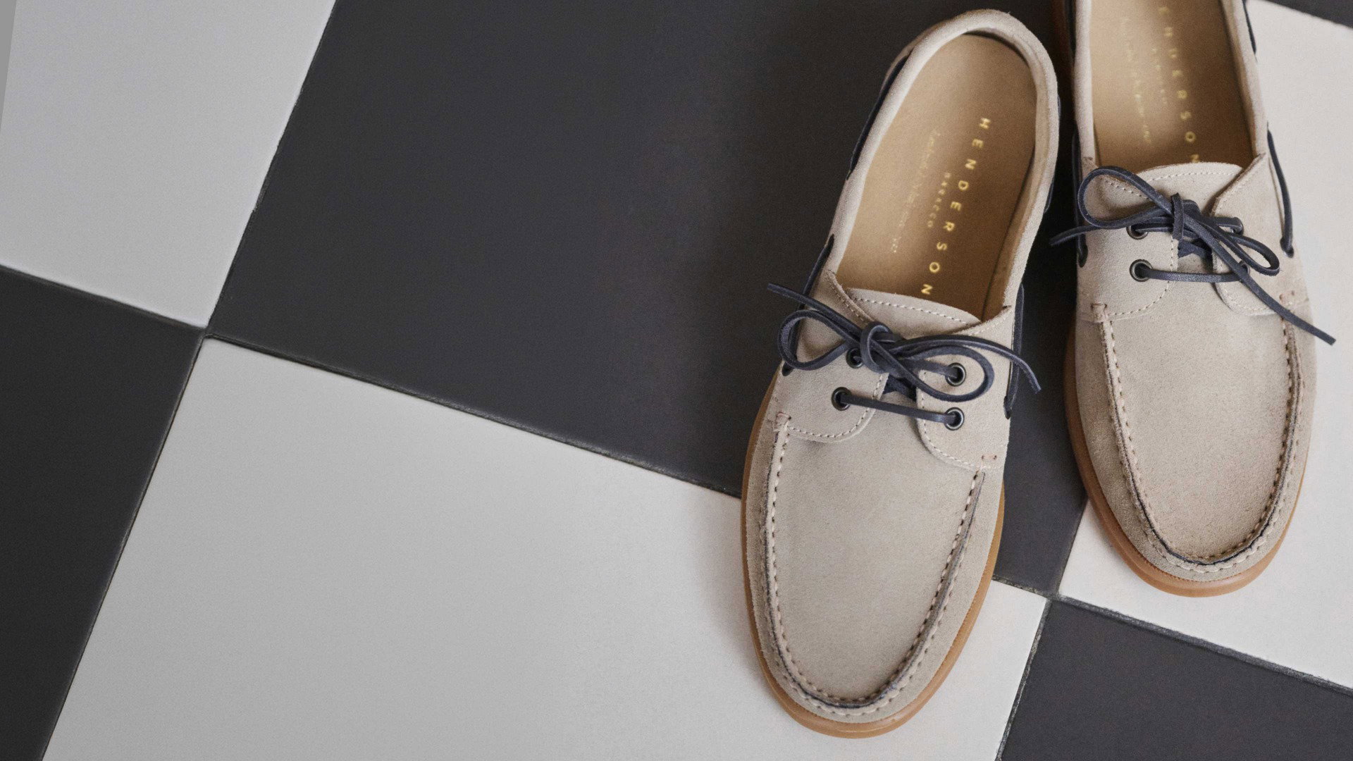 Beige Wildleder-Schuhe mit dunkelblauen Schnürsenkeln auf schwarz-weiß kariertem Boden aus Fliesen. Beige Wildleder-Schuhe mit dunkelblauen Schnürsenkeln auf schwarz-weiß kariertem Boden aus Fliesen.