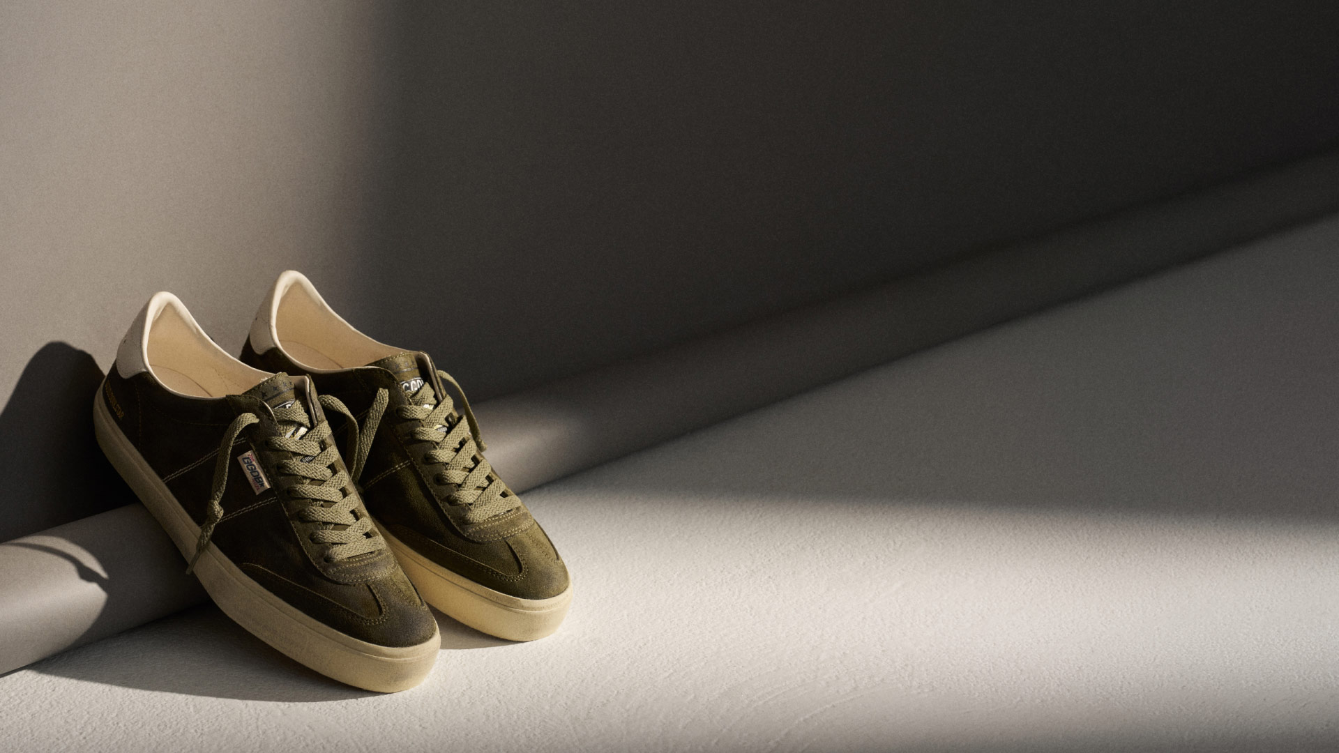 Grüne Wildleder-Sneaker mit beigen Sohlen und Schnürsenkeln, stehend auf hellem Boden mit Schatten im Hintergrund. Grüne Wildleder-Sneaker mit beigen Sohlen und Schnürsenkeln, stehend auf hellem Boden mit Schatten im Hintergrund.