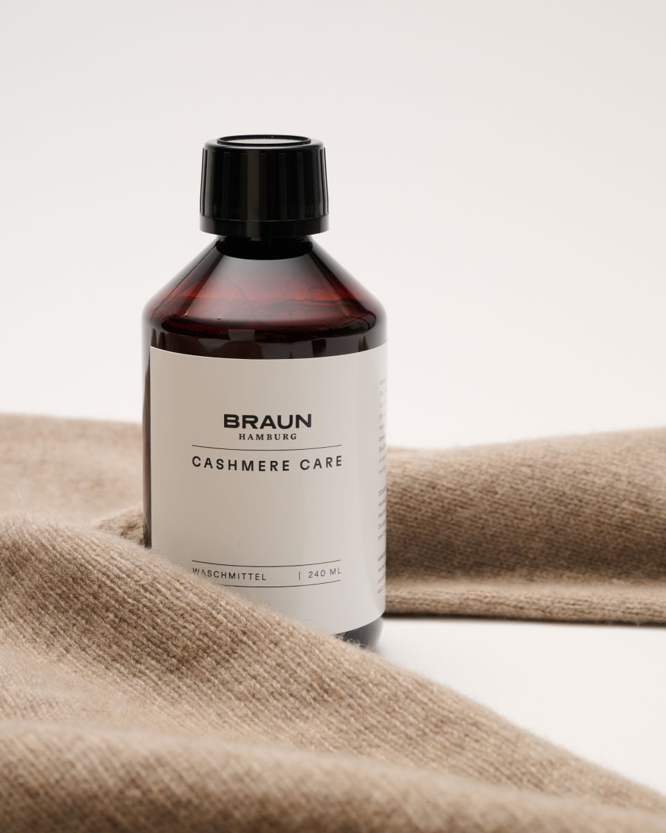 Braune Flasche mit schwarzem Deckel und Etikett 'Braun Hamburg Cashmere Care Waschmittel 240 ml' auf beigem Kaschmirstoff.