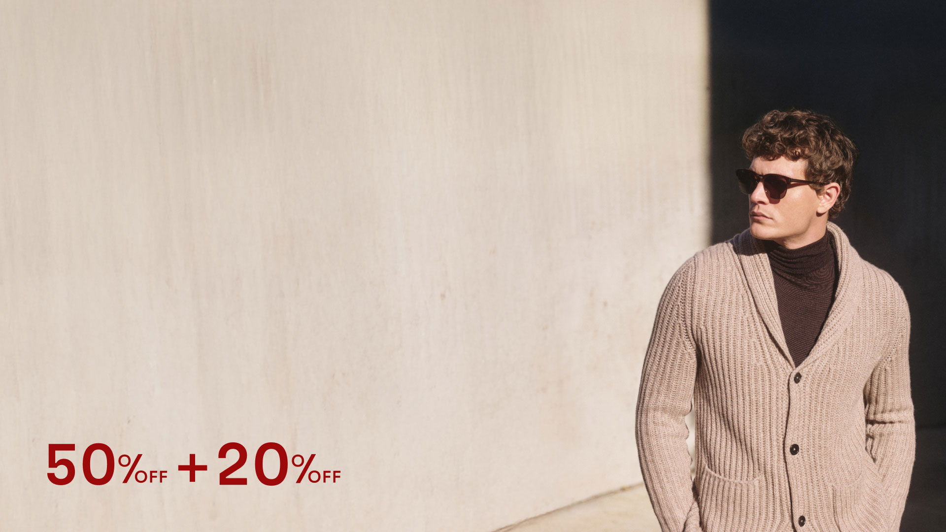 Mann mit dunkler Sonnenbrille trägt beige grob gestrickten Cardigan über schwarzem Rollkragenpullover vor heller Wand. Mann mit dunkler Sonnenbrille trägt beige grob gestrickten Cardigan über schwarzem Rollkragenpullover vor heller Wand.