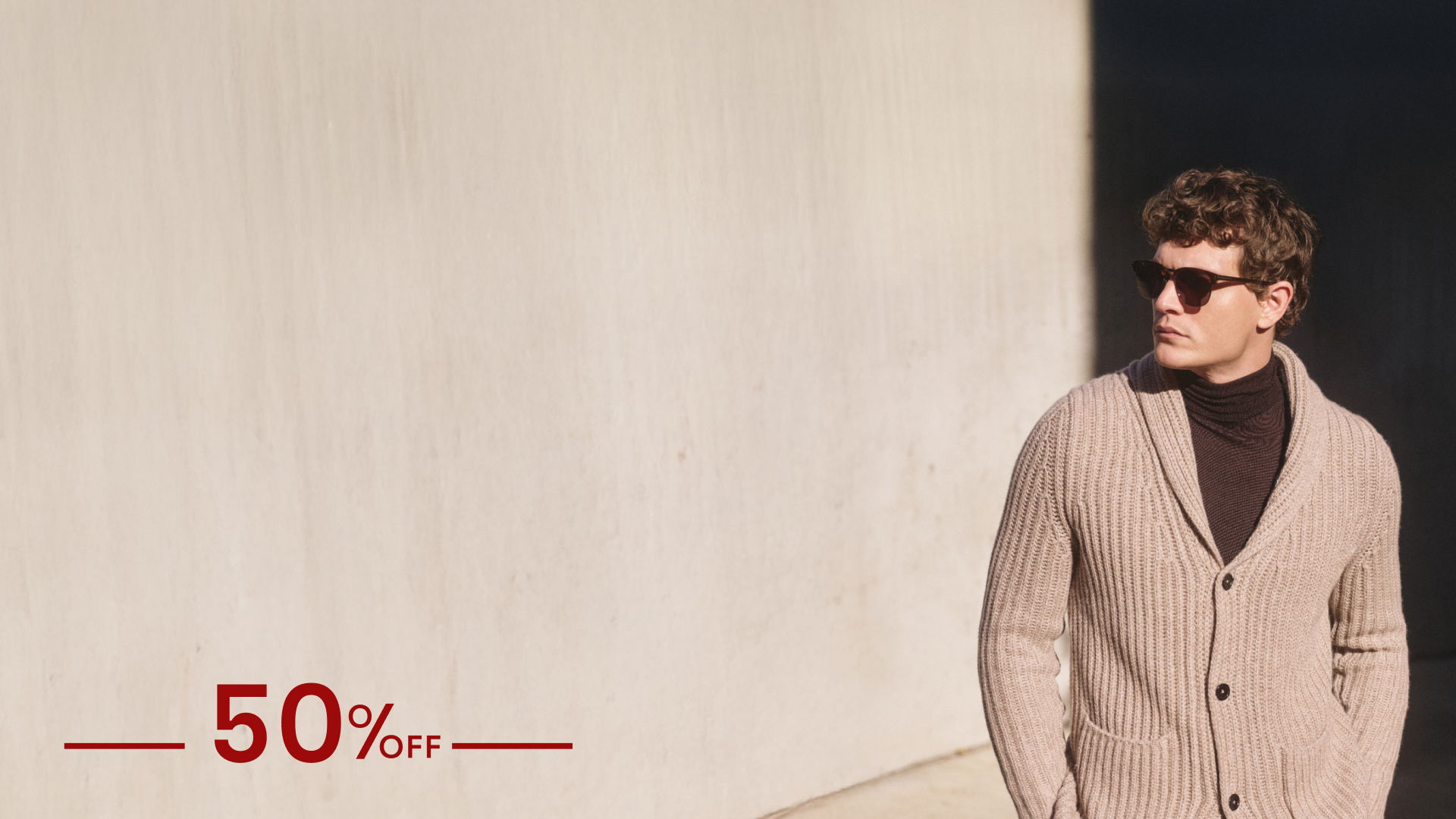 Mann mit dunkler Sonnenbrille trägt beigen Strickcardigan und schwarzen Rollkragenpullover, 50% Rabatt Schriftzug links. Mann mit dunkler Sonnenbrille trägt beigen Strickcardigan und schwarzen Rollkragenpullover, 50% Rabatt Schriftzug links.