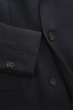 Nahaufnahme des Corneliani Woll-Kurzmantels navy aus leicht elastischer Schurwolle mit tonalem Fischgrat, Knöpfen und Pattentasche, Detail von Ärmel und Vorderseite.