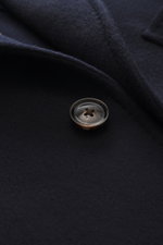 Close-up photo from above of a single button and fabric texture of the Mandelli Jacke navy, showcasing pure virgin wool, smooth feel, slim fit, two-way zipper, buttoned wind flap, stand-up collar, buttoned sleeve cuffs, half-lined interior, and two inner 