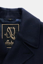 Close-up front view of the collar and label of the Sealup Pea coat 'Amalfi Peacoat' navy, a slim-fit, double-breasted pea coat made of pure wool with soft feel and lightweight padding, featuring a wide lapel collar, slanted hip pockets, small metal logo, 