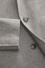 Tagliatore Mantel hellgrau meliert, Detailaufnahme von vorne oben, reine Schurwolle, Slim Fit, Drei-Knopf-Stil, fallendes Revers mit Logo-Pin, weicher Griff, Brusttasche und schräge Leistentaschen sichtbar.