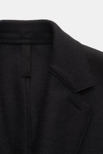 Close-up front view of the Harris Wharf London Wool coat black collar, made of heavy, pure felted virgin wool with a notch collar and slanted welt pocket detail.