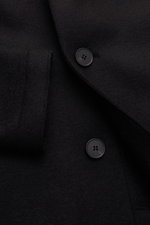 Close-up front view of Harris Wharf London Wool coat black showing heavy felted virgin wool texture, three-button placket, notch collar, and slanted welt pocket. Timeless, pure, and well thought out: This unlined coat with a straight silhouette from HARRI