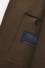 Harris Wharf London Wollmantel braun, Detailaufnahme von ungefütterter Schurwolle mit Knopf, Raw-Edge-Finish und Markenlabel, Nahansicht