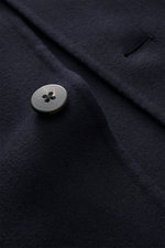 Close-up image from a top angle of the navy 04651/ A trip in a bag Coat 'Double Coat' showing a black button and detailed wool fabric texture, mix of virgin wool and microfiber, soft touch, slim fit, turn-down collar, five-button placket, slanted welt poc