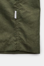 Close-up of the lower section of the 04651/ A trip in a bag Mantel 'Travel Coat' oliv, showing the olive green microfiber fabric and a small white tag with "04651" from a front-facing perspective.

<p>Praktisch unterwegs mit 04651/ A TRIP IN A BAG: Mit di