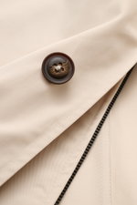 Close-up front detail of the Fay Coat 'Morning' sand showing pure cotton twill fabric, zip double front, concealed button placket, and signature button from a top angle.