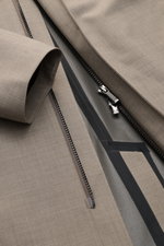 Close-up, top-down view of the zipper area of the UBR Rain coat 'Sky Fall Savile' taupe mottled, showing taupe mottled fabric with black waterproof zippers and taped seams. 

<p>The incredibly lightweight rain coat 'Sky Fall Savile' by UBR is made of smar