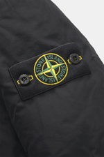 Nahaufnahme des typischen Kompass-Badges am Ärmel des Stone Island Daunen-Kurzmantels "Micro Reps" schwarz, gefertigt aus hochwertiger Microfaser mit glattem Griff, wind- und wasserabweisend, Slim Fit, mit wattierter Kapuze, zwei-Wege-Reißverschluss, Wind