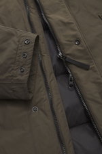 Close-up front view of Stone Island Down short coat 'Micro Reps' olive, showing high-quality microfiber, smooth feel, two-way zipper, wind flap with buttons, sleeve cuff with button, and quilted lining fabric. The coat is wind- and water-repellent, slim f