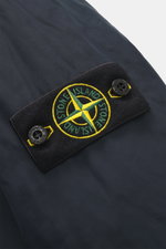 Close-up of the Stone Island Short Coat 'Micro Reps' navy showing the typical compass badge on high-quality microfiber with smooth touch, wind and water repellent fabric, photographed from a top-down perspective.