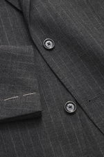 Close-up top-down view of the Lardini Anthracite striped suit jacket showing its pure new wool fabric, subtle check pattern, tailored two-button style, notched lapel with floral pin, classic breast pocket, patch hip pockets, and unfinished sleeve cuffs wi