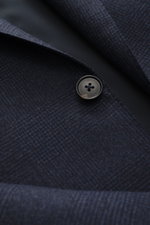Close-up front view of the Zegna Suit 'Trofeo' navy melange showing a subtle check pattern, pure wool fabric, soft touch, slim fit, and a black button.