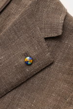 Nahaufnahme des Belvest Sakko graubraun meliert aus Leinen und Wolle, Slim Fit, taillierter Drei-Knopf-Stil, fallendes Revers mit bunter Anstecknadel, fotografiert von schräg oben.